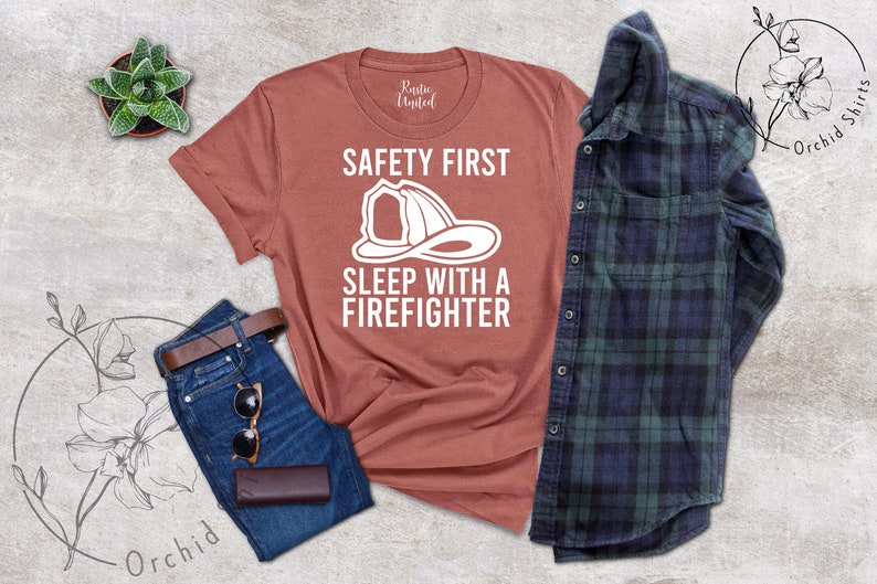 May include: A rust-colored t-shirt with a white graphic of a firefighter helmet and the text "Safety First Sleep with a Firefighter".