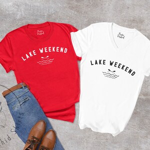 以下が含まれることがあります： 「LAKE WEEKEND」の文字とオールと波のグラフィックがプリントされた赤と白のTシャツ2枚。青いジーンズと茶色の革靴と組み合わせており、カジュアルなアウトドアをテーマにしていることを示唆しています。