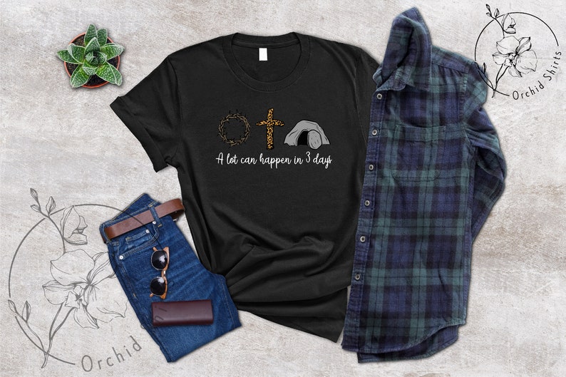 K&ouml;nnte beinhalten: Schwarzes T-Shirt mit einem Aufdruck einer Dornenkrone, einem Kreuz und einem Grab. Der Text "A lot can happen in 3 days" ist unter dem Aufdruck gedruckt.