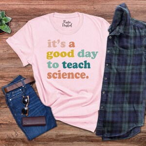 Op de afbeelding: Roze T-shirt met de tekst "it's a good day to teach science." in kleurrijk retro lettertype.