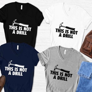 May include: Four V-neck t-shirts in black, navy blue, white, and heather gray with a black and white graphic of a hammer and the text "This is not a drill".