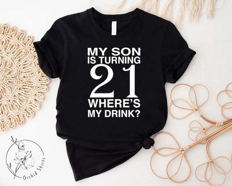 Peut inclure: T-shirt noir avec du texte blanc qui dit "Mon fils a 21 ans O&ugrave; est ma boisson ?"