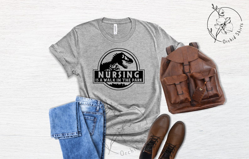 May include: A gray t-shirt with a black graphic of a dinosaur and the text "Nursing is a walk in the park".
