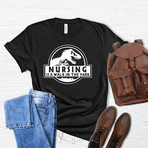 May include: Black t-shirt with a white graphic of a dinosaur and the text "Nursing is a walk in the park".