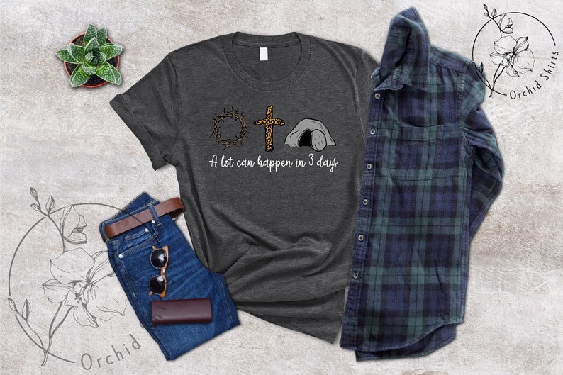 K&ouml;nnte beinhalten: Ein dunkelgraues T-Shirt mit einem Motiv aus einer Dornenkrone, einem Kreuz mit Leopardenmuster und einem Grab. Der Text "A lot can happen in 3 days" ist unter dem Motiv gedruckt.