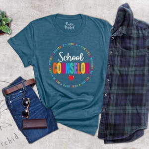 May include: Teal blue t-shirt with a colorful circle graphic that says "School Counselor" with the words "Kind, Caring, Dedicated,  Warm,  Love, Fun, Go, Passion,  Relax" around the circle.