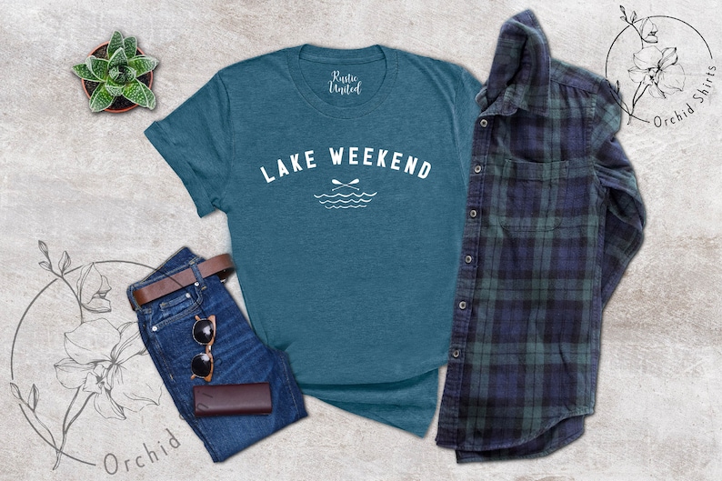 以下が含まれることがあります： 「LAKE WEEKEND」の白文字とオールと波のグラフィックが入った、ティール色のTシャツ。青いジーンズ、茶色のベルト、サングラス、茶色の財布と組み合わせています。チェック柄のシャツも含まれています。