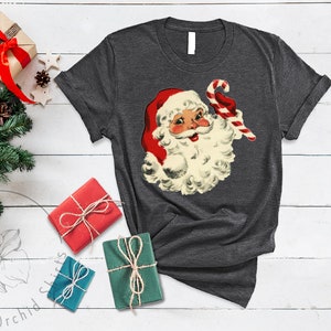 May include: A dark gray t-shirt with a vintage illustration of Santa Claus holding a candy cane. The illustration is in red, white, and green colors.