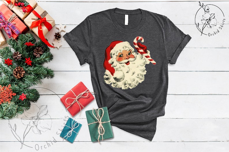 May include: A dark gray t-shirt with a vintage illustration of Santa Claus holding a candy cane. The illustration is in red, white, and green colors.