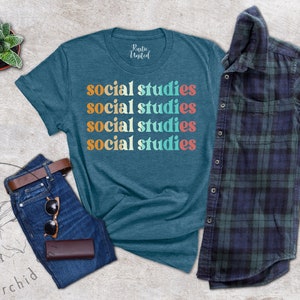 May include: Teal t-shirt with the words "social studies" in a retro font. The shirt is paired with blue jeans, a brown belt, sunglasses, and a wallet. A plaid shirt and a small potted plant are also in the image.
