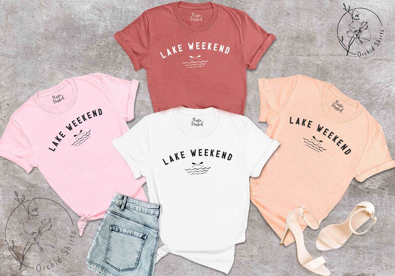 以下が含まれることがあります： ピンク、白、ピーチ、ラストカラーの半袖Tシャツ5枚。各シャツには、「LAKE WEEKEND」の文字と、オールと波のグラフィックが描かれています。シャツは、デニムショーツとサンダルと一緒に表示されています。