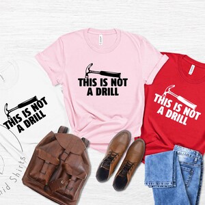 May include: Three t-shirts with the text "This is not a drill" and a hammer graphic. The shirts are white, pink, and red.