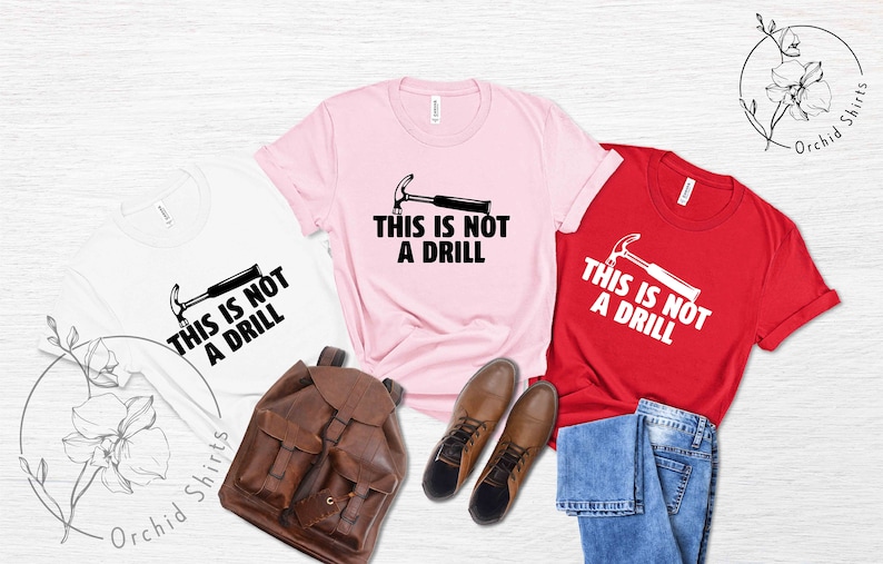 May include: Three t-shirts with the text "This is not a drill" and a hammer graphic. The shirts are white, pink, and red.