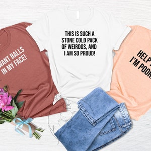 May include: Three t-shirts with humorous phrases in black text. One is brick red and says "I WANT BALLS IN MY FACE!". The second is white and says "THIS IS SUCH A STONE COLD PACK OF WEIRDOS, AND I AM SO PROUD!". The third is peach and says "HELP ME I'M POOR!".