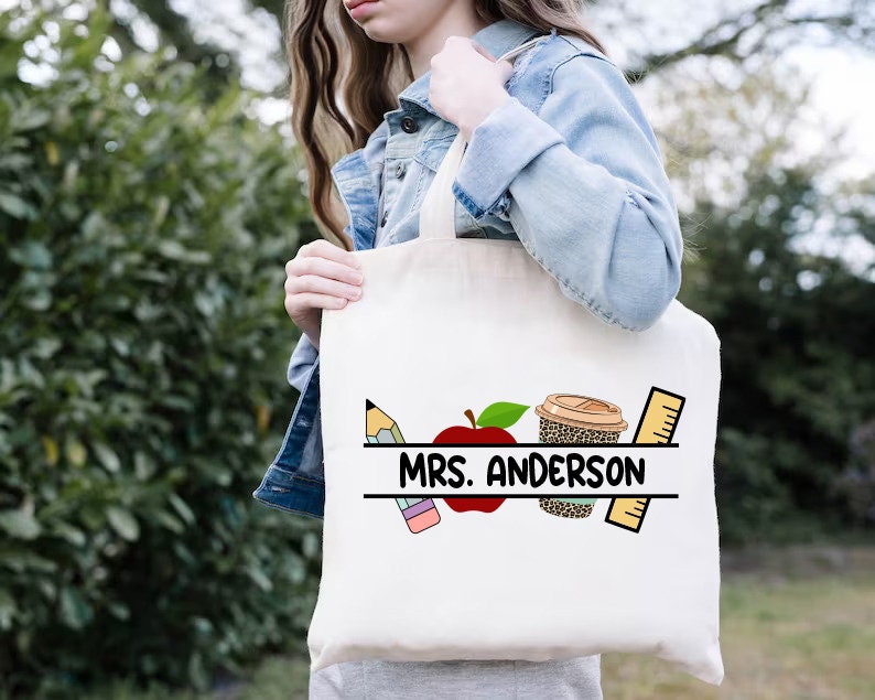 Może przedstawiać: Biała torba typu tote z czarno-białym nadrukiem oł&oacute;wka, jabłka, kubka do kawy i linijki. Na torbie nadrukowany jest tekst "MRS. ANDERSON".