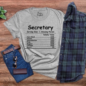 May include: A heather gray t-shirt featuring black text that reads Secretary, Serving Size: 1 Amazing Person, and a nutrition facts label listing Hard Work, Passion, Determination, Pride, Respect, Caffeine, and Regret with their percentages.