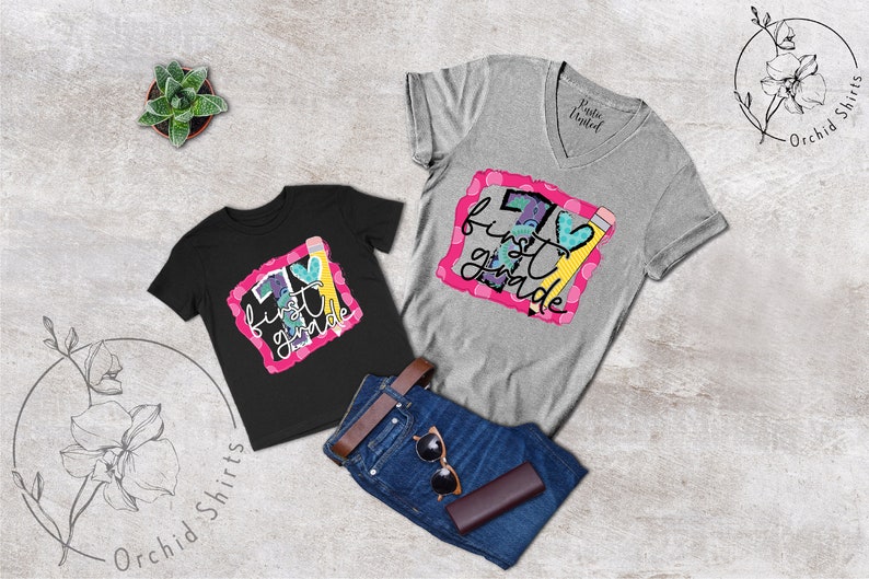 May include: Two t-shirts with the text "I love first grade" in a colourful design. The shirts are black and grey and have a heart and pencil graphic.