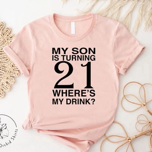a pink shirt that says, my son is turning 21 where's my drink
