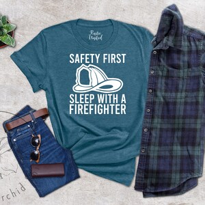 May include: A teal blue t-shirt with the text "Safety First Sleep with a Firefighter" and a white illustration of a firefighter's helmet.