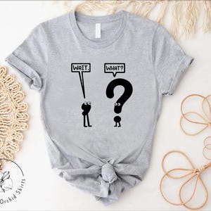 May include: A gray t-shirt with a black graphic of two stick figures. The first stick figure says "Wait." and the second stick figure says "What?" and is shaped like a question mark.