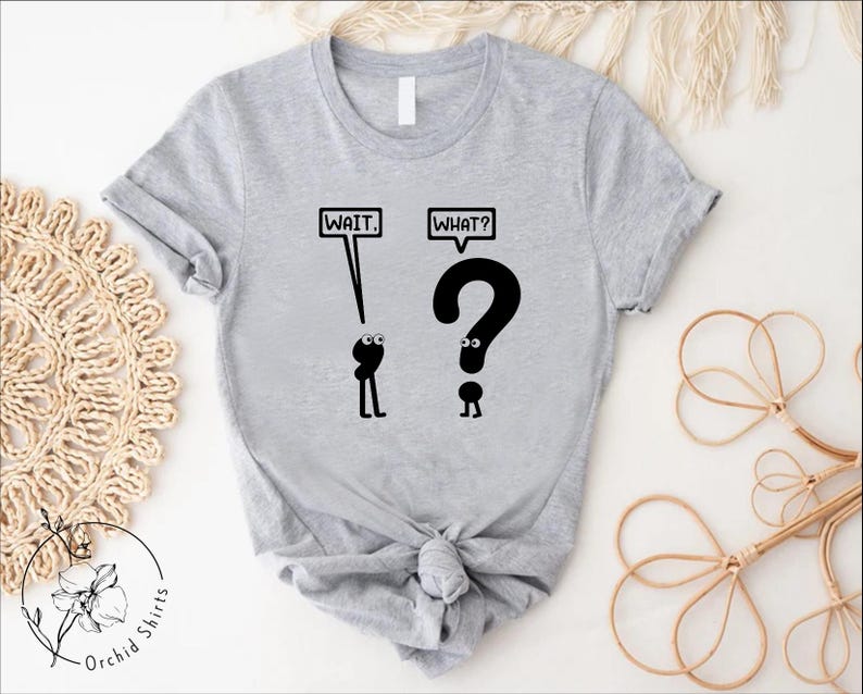 May include: A gray t-shirt with a black graphic of two stick figures. The first stick figure says "Wait." and the second stick figure says "What?" and is shaped like a question mark.