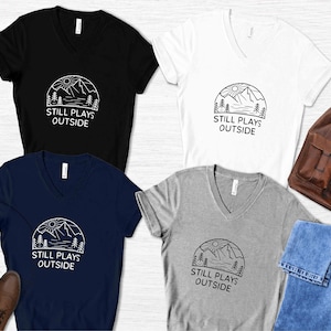May include: Four V-neck t-shirts in black, white, navy blue, and heather gray with a graphic of a mountain range and the text "Still Plays Outside".