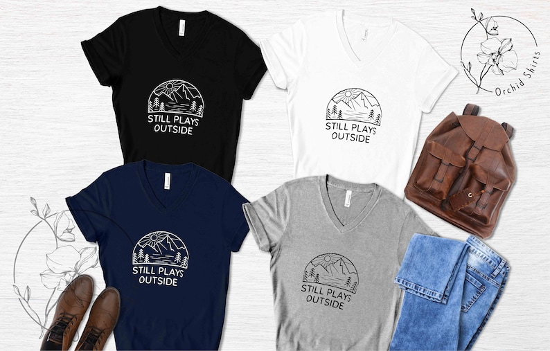 May include: Four V-neck t-shirts in black, white, navy blue, and heather gray with a graphic of a mountain range and the text "Still Plays Outside".