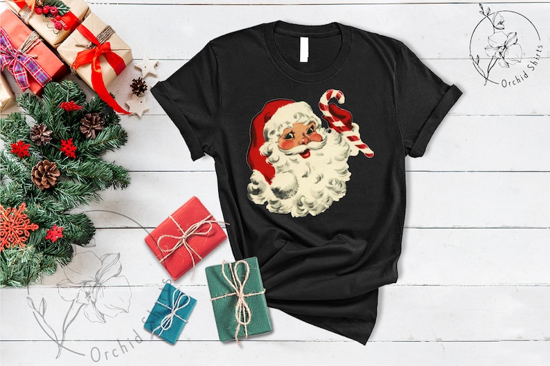 May include: Black t-shirt with a vintage illustration of Santa Claus holding a candy cane. The illustration is in red, white, and green.