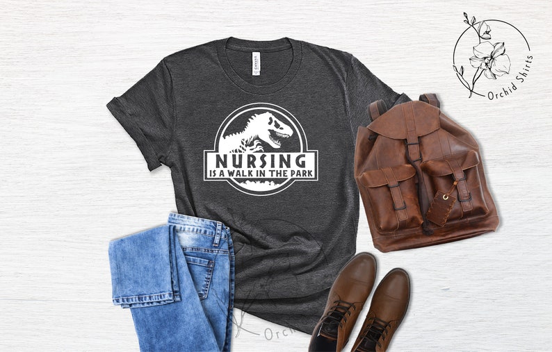 May include: A dark gray t-shirt with a white graphic of a dinosaur and the text "Nursing is a walk in the park".