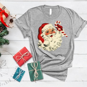 May include: A gray t-shirt with a vintage illustration of Santa Claus holding a candy cane. The illustration is in red, white, and cream colors.