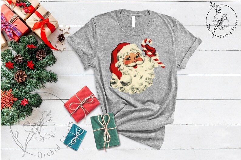 May include: A gray t-shirt with a vintage illustration of Santa Claus holding a candy cane. The illustration is in red, white, and cream colors.