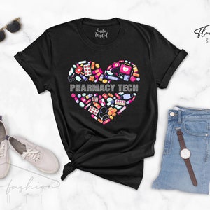 Może przedstawiać: Czarny T-shirt z sercowatym wzorem wykonanym z przedmiot&oacute;w związanych z apteką, takich jak tabletki, bandaże i stetoskop. W sercu znajduje się napis "Pharmacy Tech".