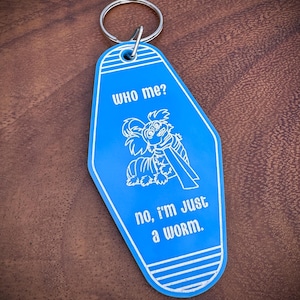 May include: A blue keychain with a silver ring. The keychain has a white illustration of a worm-like creature and the text "WHO me?" and "no, I'm just a worm."