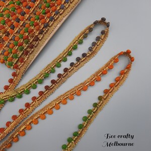 May include: Three spools of gold trim with colourful pom-poms. The trim features a repeating pattern of small, round pom-poms in shades of orange, green, and blue.