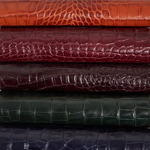 May include: Five pieces of leather stacked on top of each other. The leather is a variety of colors, including orange, burgundy, dark purple, dark green, and dark blue. The leather has a crocodile pattern.