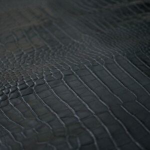 May include: Close-up of black alligator embossed leather with a textured, scaly pattern.