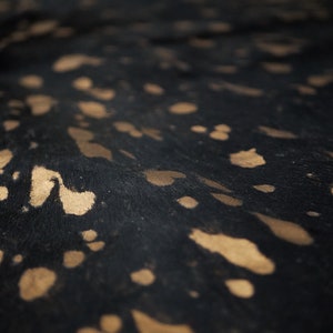 May include: Close-up of a black and gold cowhide with a spotted pattern. The hide has a soft, fuzzy texture.