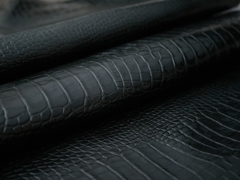 May include: Close-up of black alligator leather with a textured, scaly pattern.