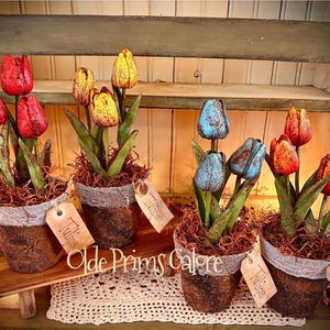 May include: Arrangement of artificial tulips in rustic pots. The tulips are in shades of red, yellow, and blue, with green leaves. Each pot is wrapped with burlap and has a tag that says "Tulips". The arrangement is on a wooden shelf.