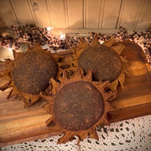 May include: Three brown dried sunflower heads on a wooden tray. The sunflowers are arranged in a circle with the stems facing outwards. The tray is made of dark wood and has a natural finish.