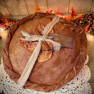 May include: A brown fabric pie with a rustic look, decorated with cinnamon sticks and dried apple slices. The pie is tied with twine and has a metal tag that says "Apple".