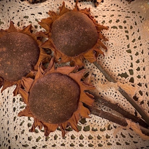 May include: Three brown felt sunflowers with brown stems on a white crocheted doily.