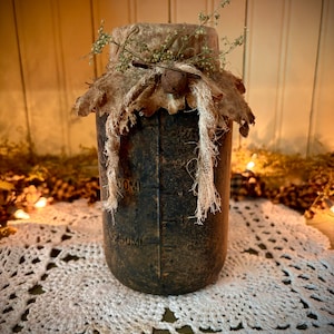 May include: A rustic, brown glass jar with a burlap lid and twine accents. The jar has markings for 250ml and 50ml. The jar is sitting on a white crocheted doily.