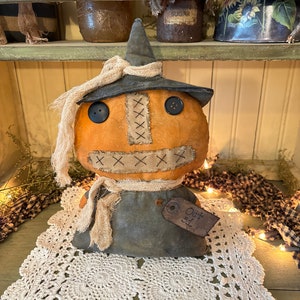 May include: A handmade rag doll pumpkin with a black witch hat, stitched X's for a mouth, and a brown tag that says "Oct 31". The doll is sitting on a white crocheted doily.