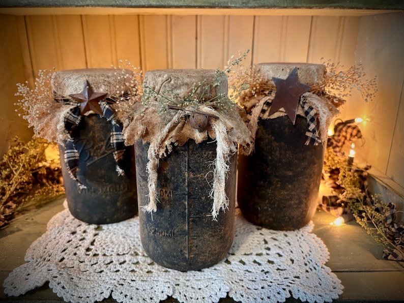 May include: Three rustic mason jars decorated with burlap, lace, and small metal stars. The jars are sitting on a white crocheted doily.