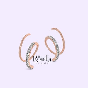 May include: A pair of rose gold spiral earrings featuring a curved design with a row of small, clear, sparkling stones set along the front edge. The text Rosella JEWELS is printed in black between the two earrings on a light purple background.