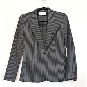 May include: A gray and black striped blazer with a notched lapel, long sleeves, and a two-button closure. The blazer is hanging on a black hanger against a white background. The blazer has a small label on the back of the neck.