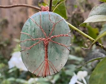 May include: A copper wire tree of life design wrapped around a light green oval-shaped stone pendant.