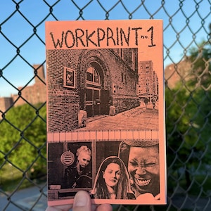 May include: A pink zine titled "WORKPRINT-1" with black illustrations. The cover features a drawing of a building and the bottom half shows three people. The zine is held in front of a chain-link fence.