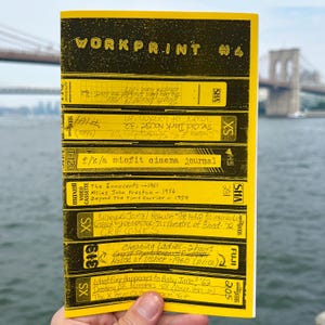 May include: A yellow zine titled "WORKPRINT #4" featuring a collage of VHS tape labels with handwritten text. The zine is held in front of a blurred background of a bridge and water.
